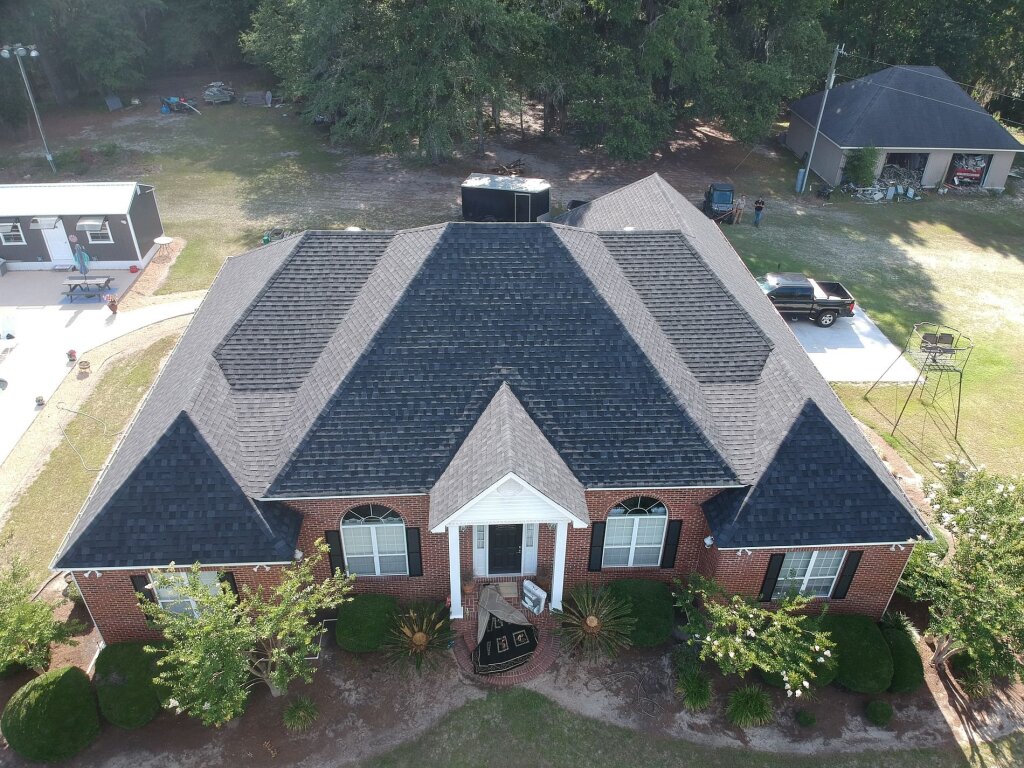 Aerial view of brick ranch home with gray shingle roof and white columned entrance