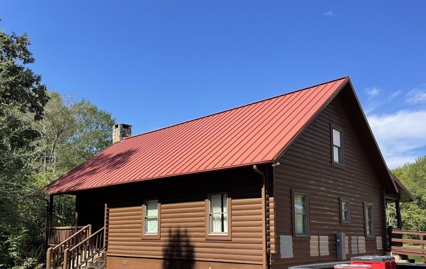 Log cabin with red metal roof surrounded by trees under blue sky