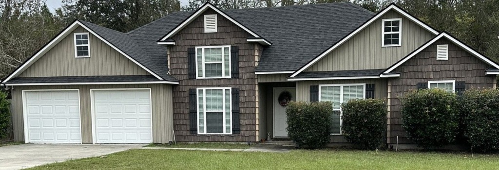 Modern single-story home with mixed siding, white garage doors, and landscaped yard