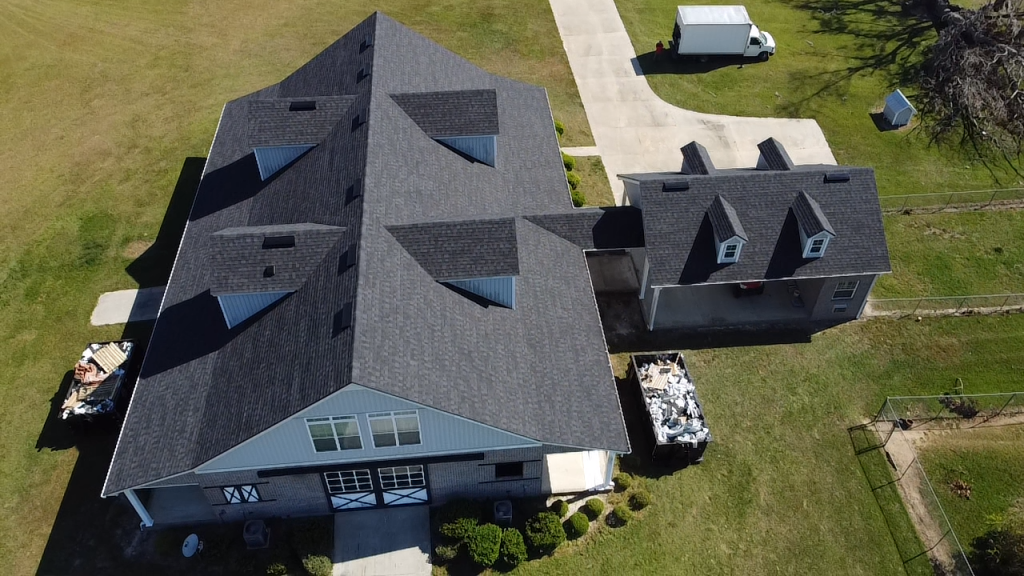Aerial view of large residential home with gray shingled roof and garage in rural setting