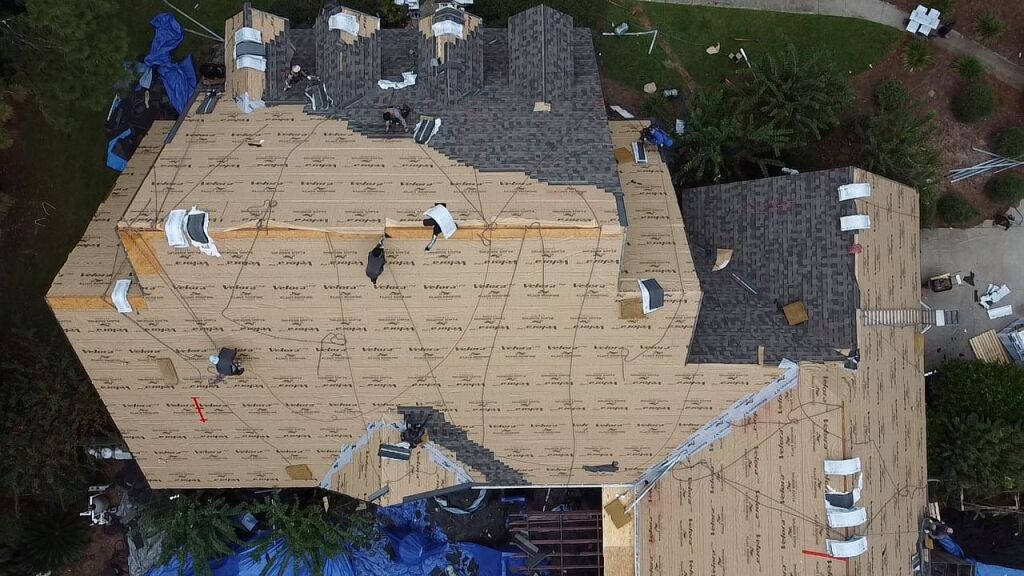 Aerial view of house roof construction with plywood decking and shingles being installed