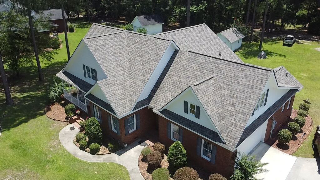Aerial view of large brick house with gray shingle roof surrounded by landscaping