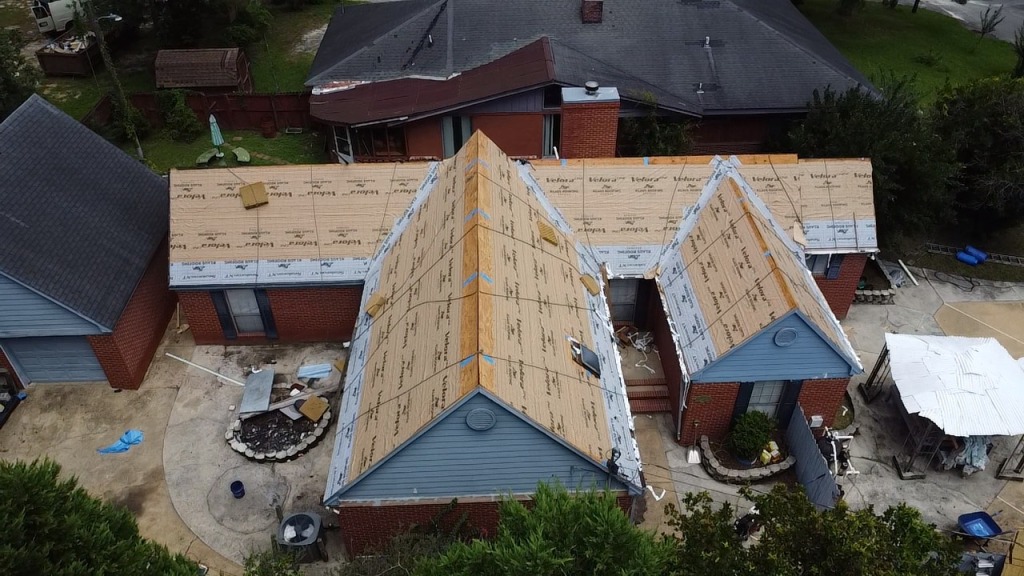 Aerial view of residential roof construction with exposed plywood sheathing and materials