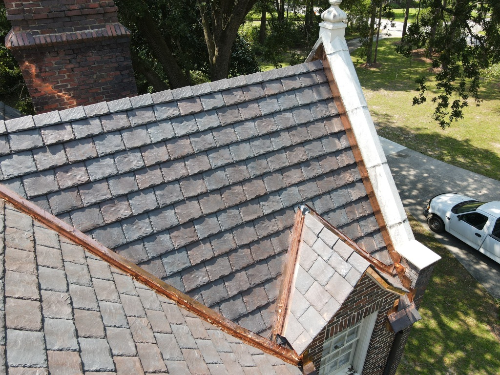 Aerial view of slate tile roof with white chimney and copper gutters on residential home