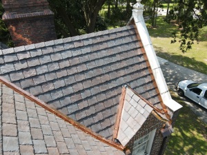 Aerial view of slate tile roof with white chimney and copper gutters on residential home