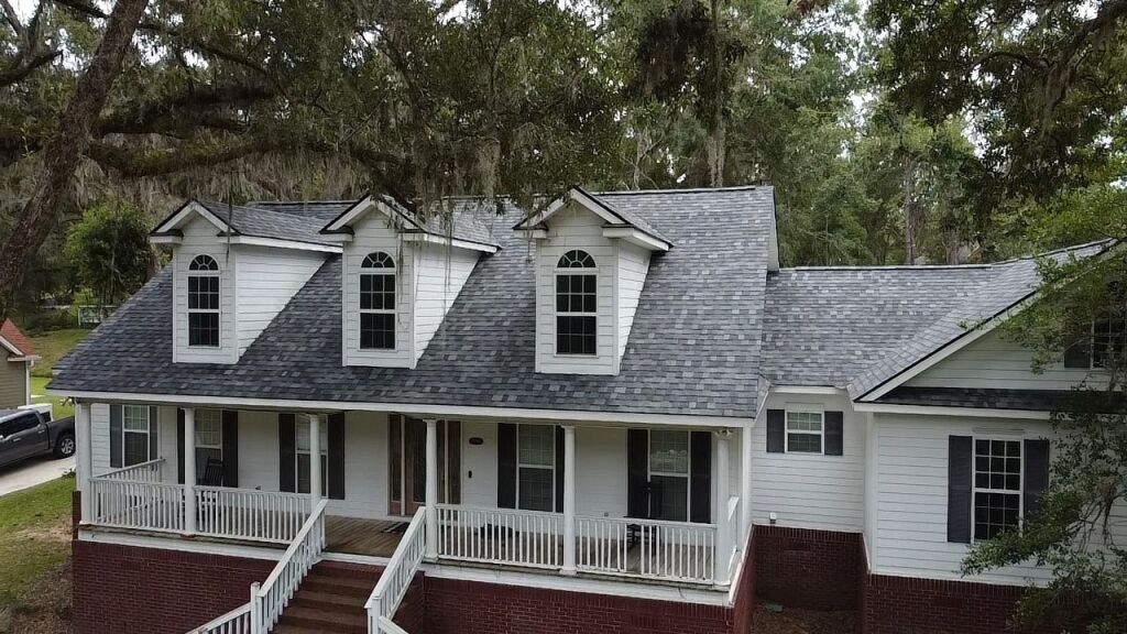 White colonial house with dormers, wrap-around porch and brick foundation