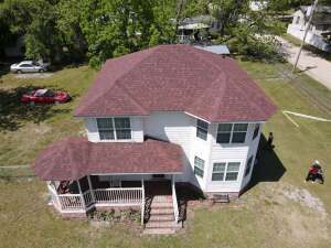 Aerial view of white two-story house with red shingle roof and front porch