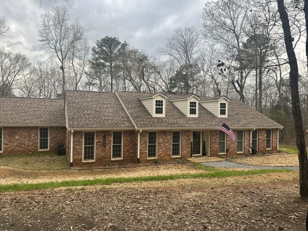 Single-story brick ranch house with three dormers and American flag in wooded area