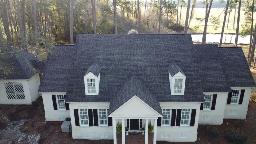 Aerial view of white colonial house with dark shingle roof and black shutters