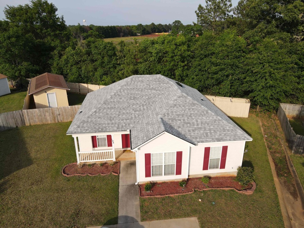 Aerial view of single-story white house with red shutters and gray shingle roof