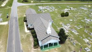 Aerial view of white church with cross-shaped roof surrounded by cemetery grounds