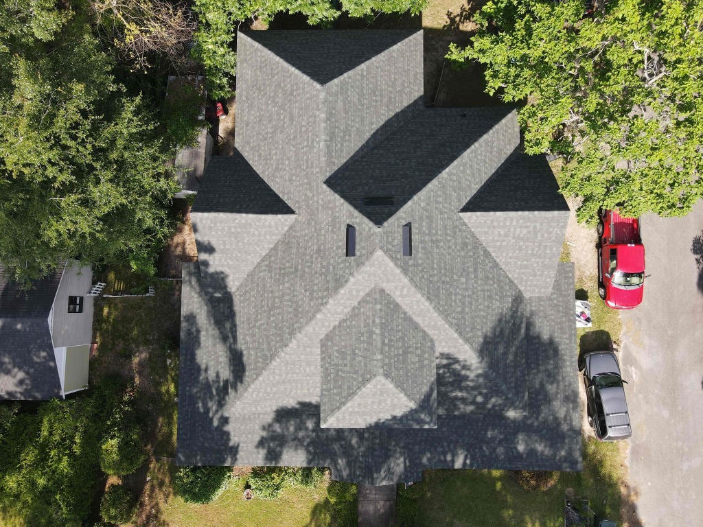 Aerial view of residential house with gray shingle roof surrounded by green trees