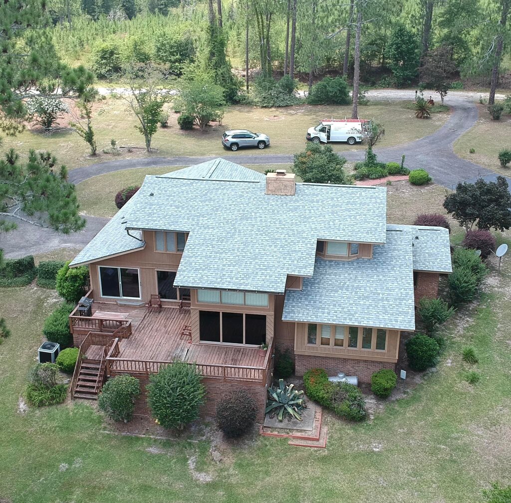 Aerial view of large two-story brick house with gray roof and wooden deck