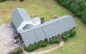 Aerial view of single-story brick house with gray shingle roof surrounded by green lawn