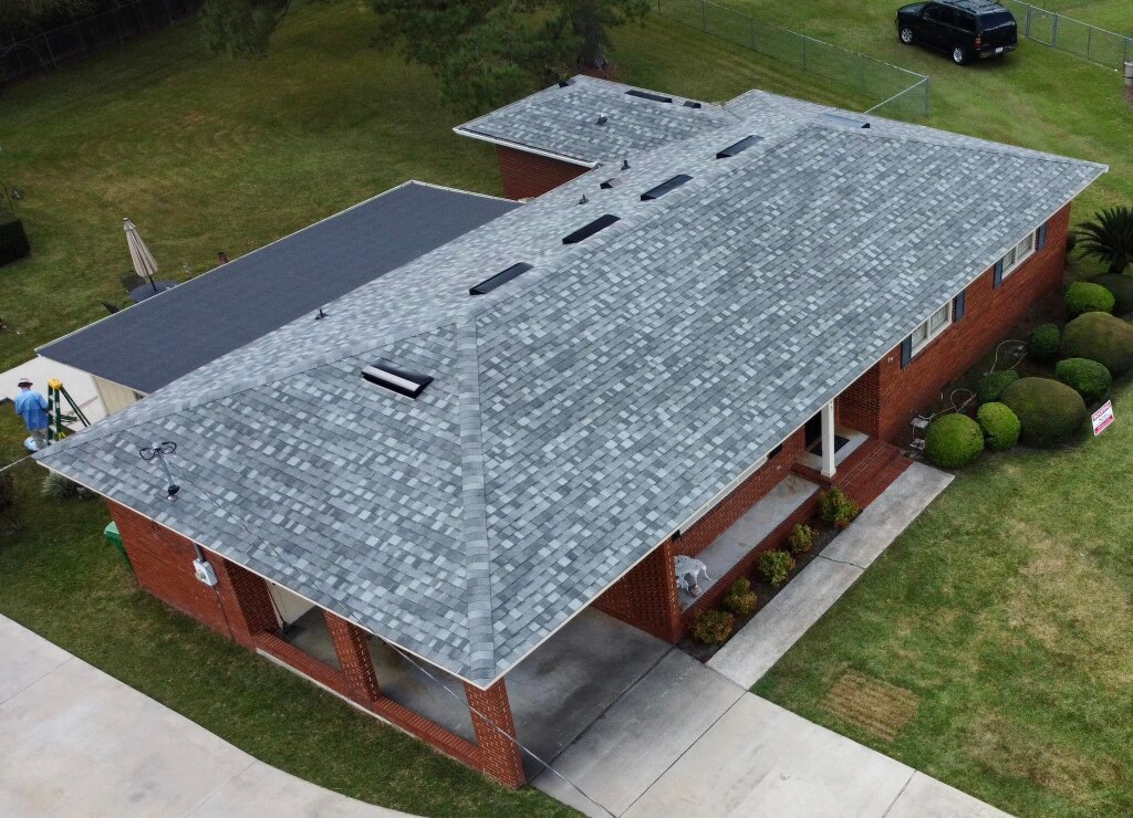 Aerial view of brick house with new gray shingle roof installation in progress