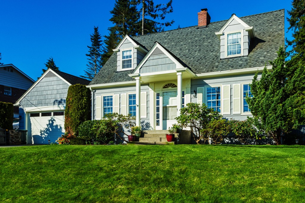 Beautiful gray Cape Cod style home with white shutters and green lawn on sunny day