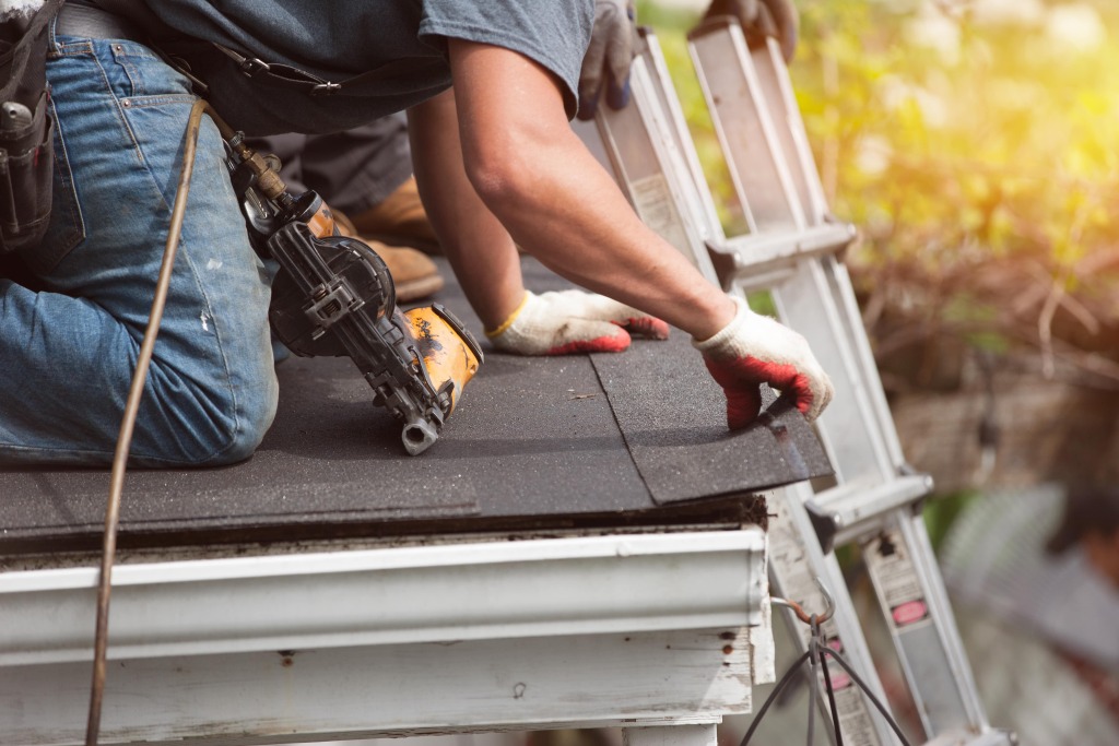 Professional roofer installing asphalt shingles with nail gun on residential roof