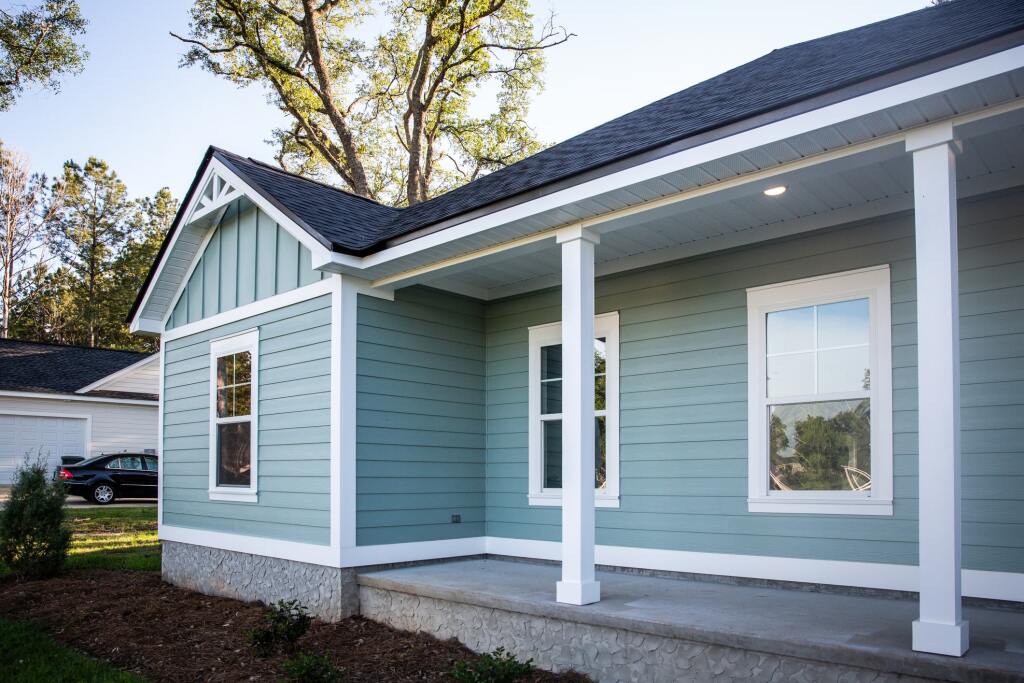 Modern sage green house with white trim and covered front porch in residential neighborhood