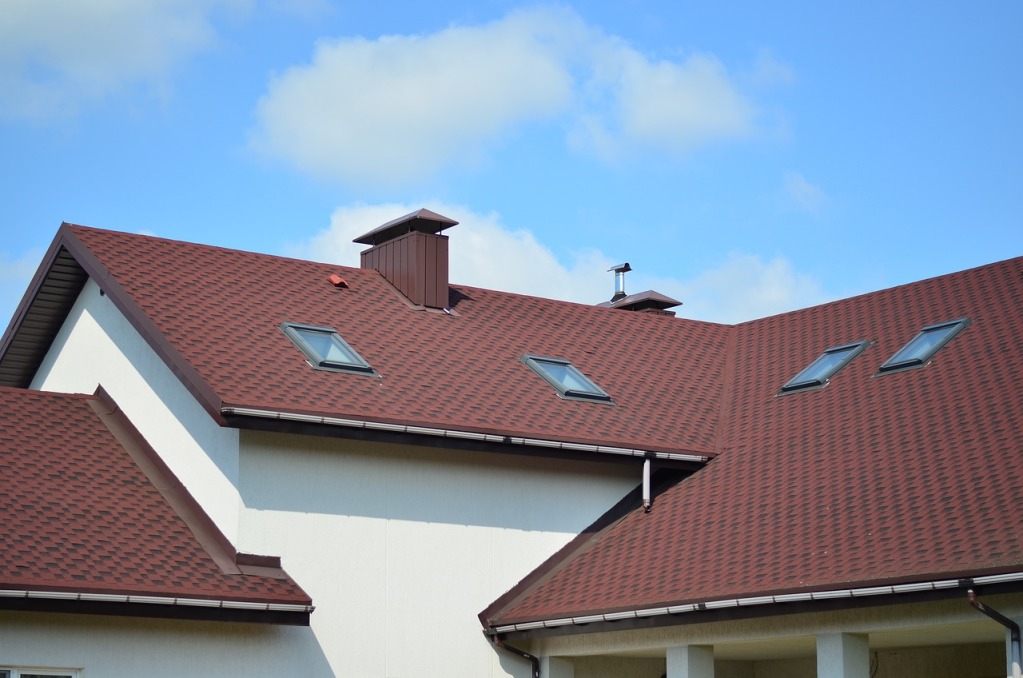 Red tile roof with skylights and chimney on modern white house against blue sky