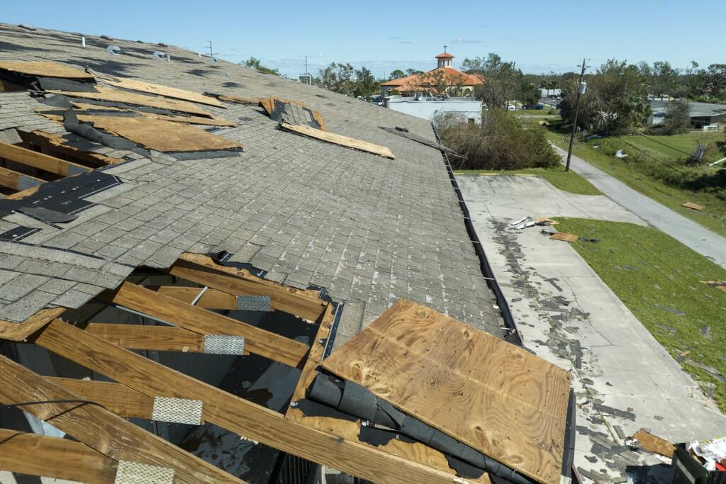 Storm damaged roof with torn shingles and exposed wood beams in residential area