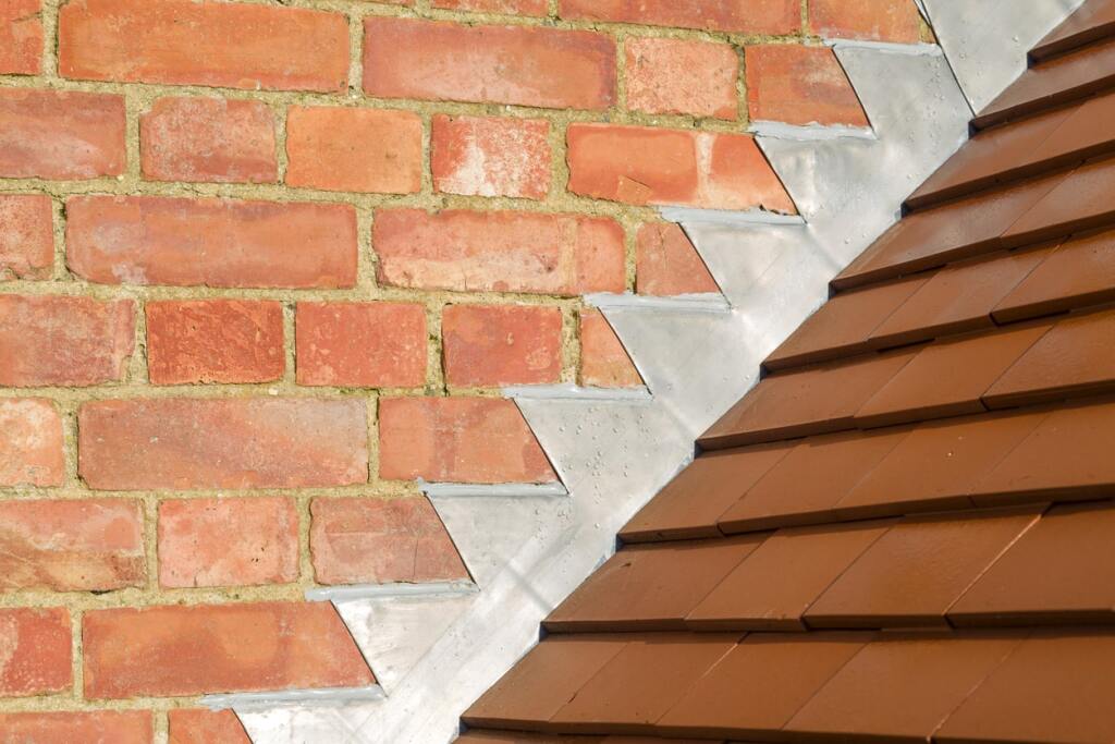 Red brick wall meets terracotta roof tiles with white mortar flashing detail