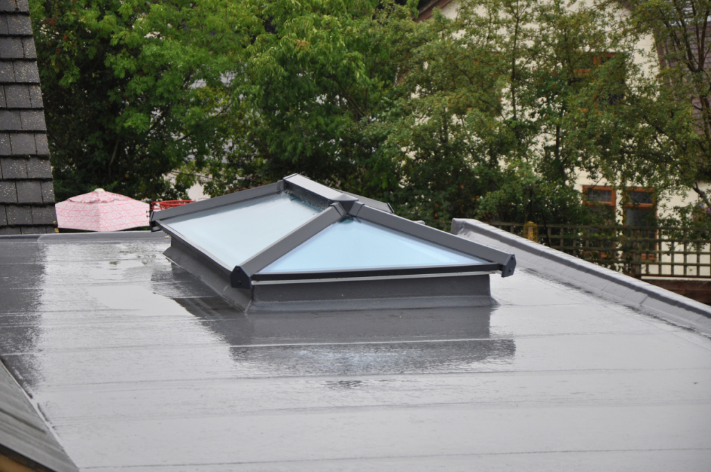 Modern glass skylight installed on flat roof membrane with residential buildings