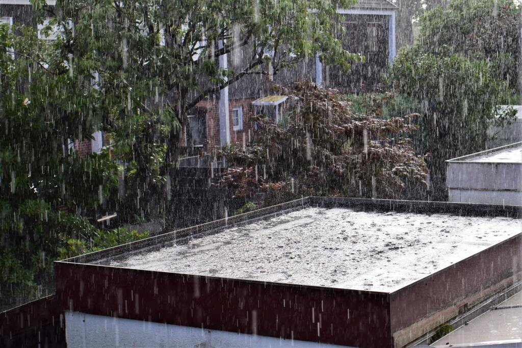 Heavy rainfall pouring down on residential rooftops and trees in neighborhood