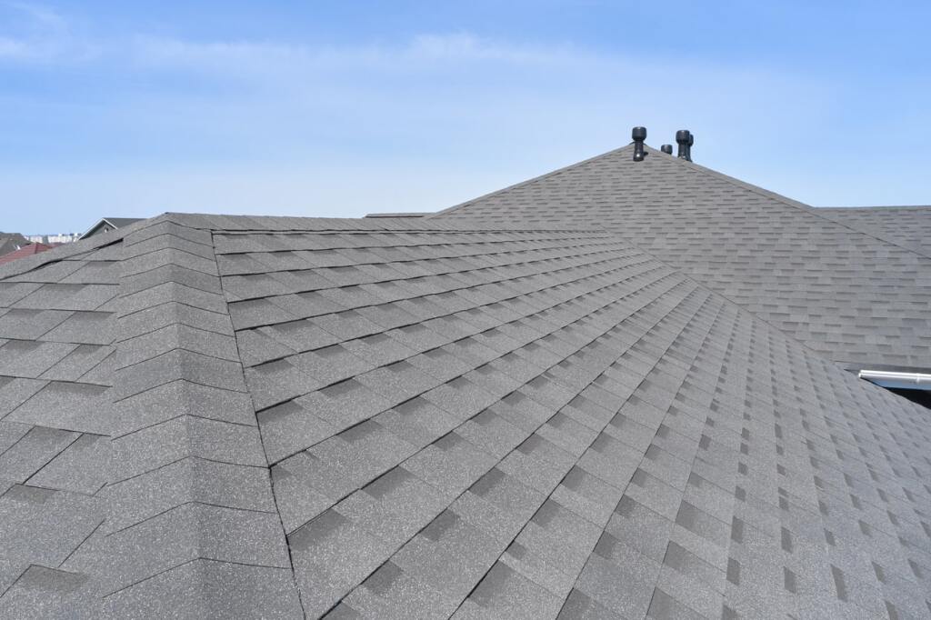 Gray asphalt shingle roof with ridge lines and chimneys against blue sky