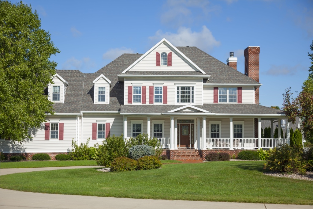 White colonial house with red shutters, wraparound porch and brick foundation