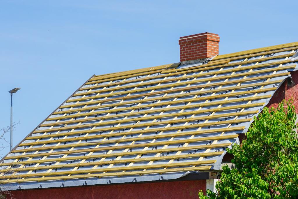 House roof under construction with wooden battens and brick chimney on clear day