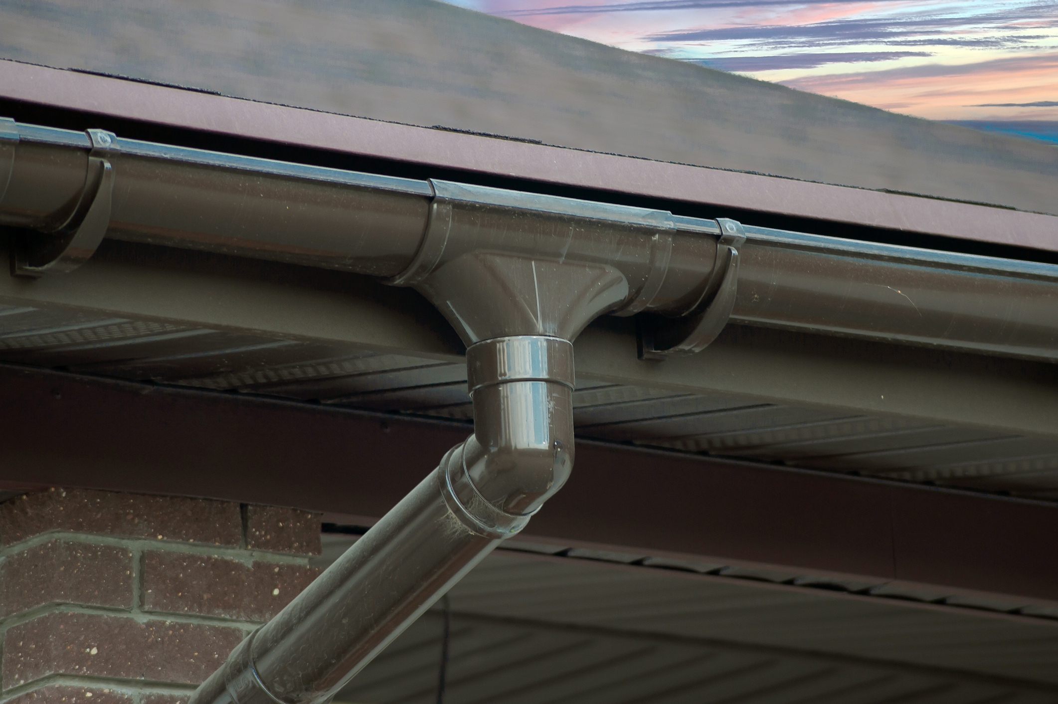 Gray metal rain gutter system with downspout attached to residential roof edge