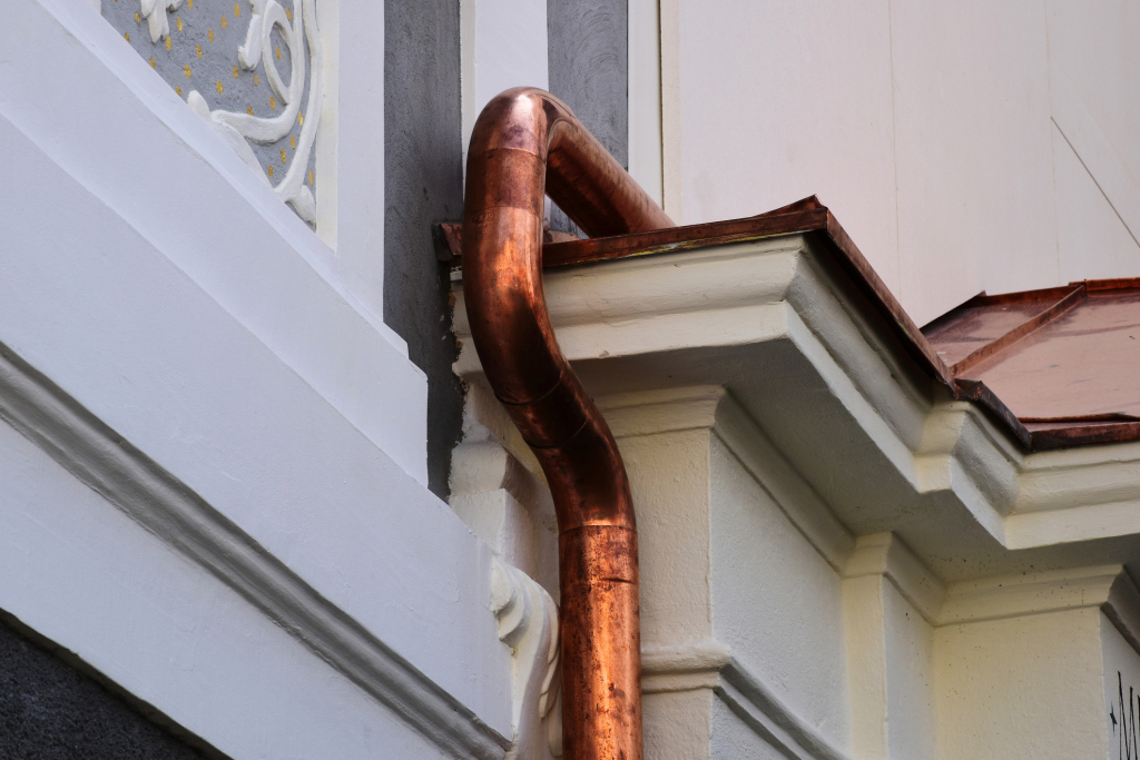 Copper downspout and gutter system on white building exterior with decorative trim