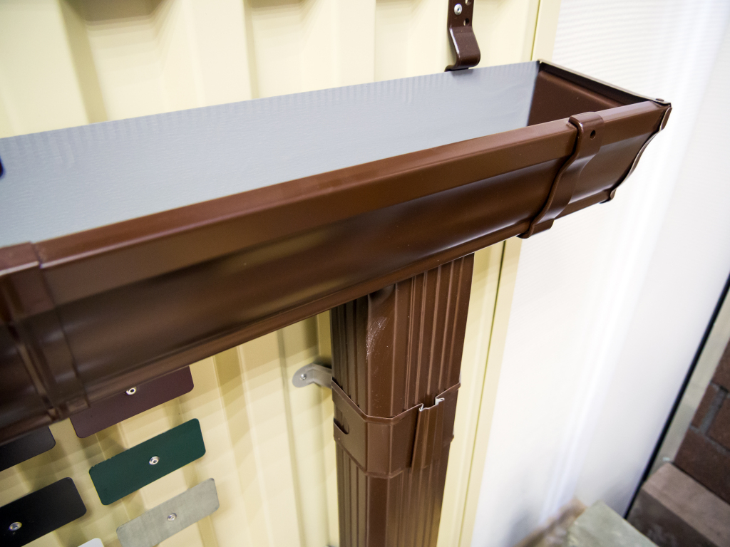 Brown plastic rain gutter system with downspout installed on building exterior
