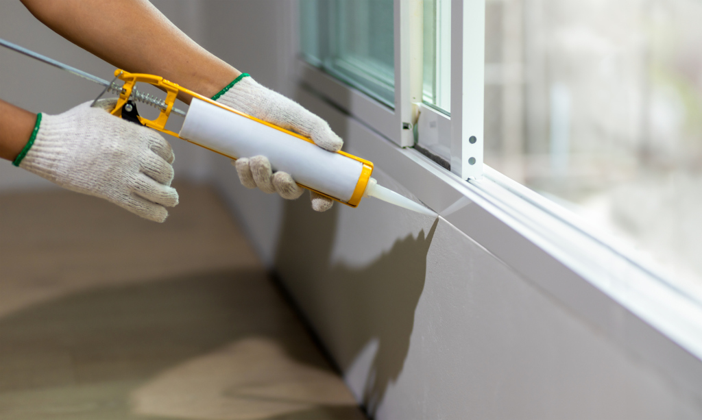 Person applying sealant to a window frame with a caulking gun.