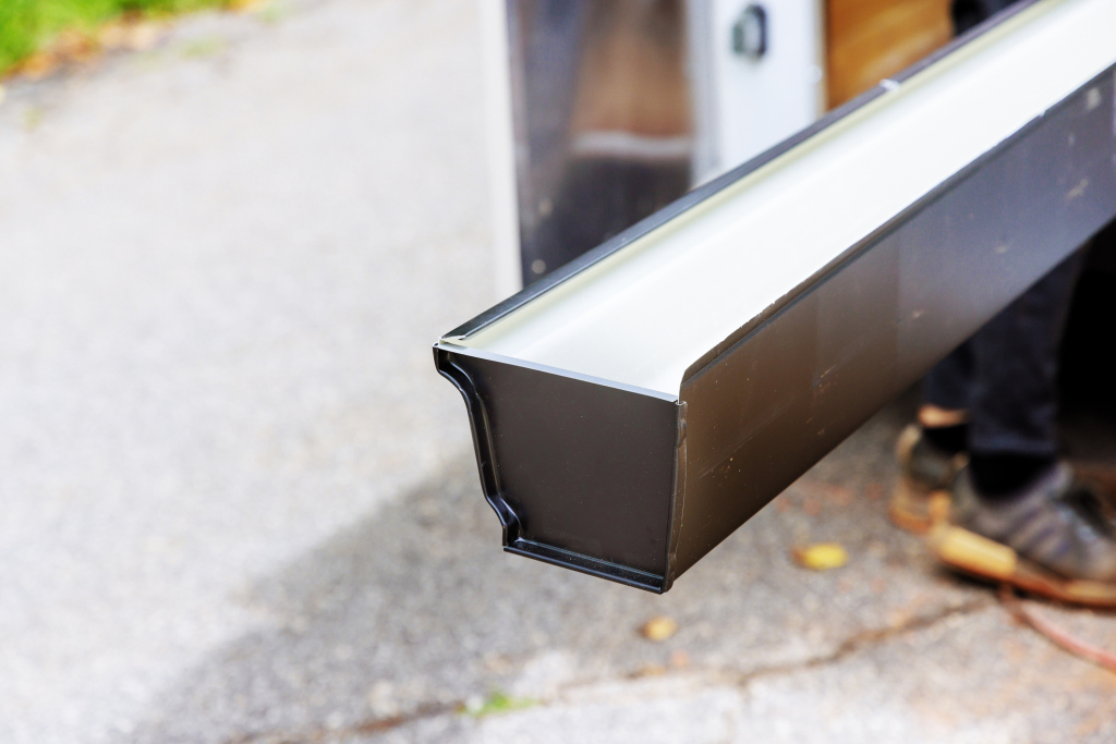 Close-up of black metal gutter downspout with white top section on concrete