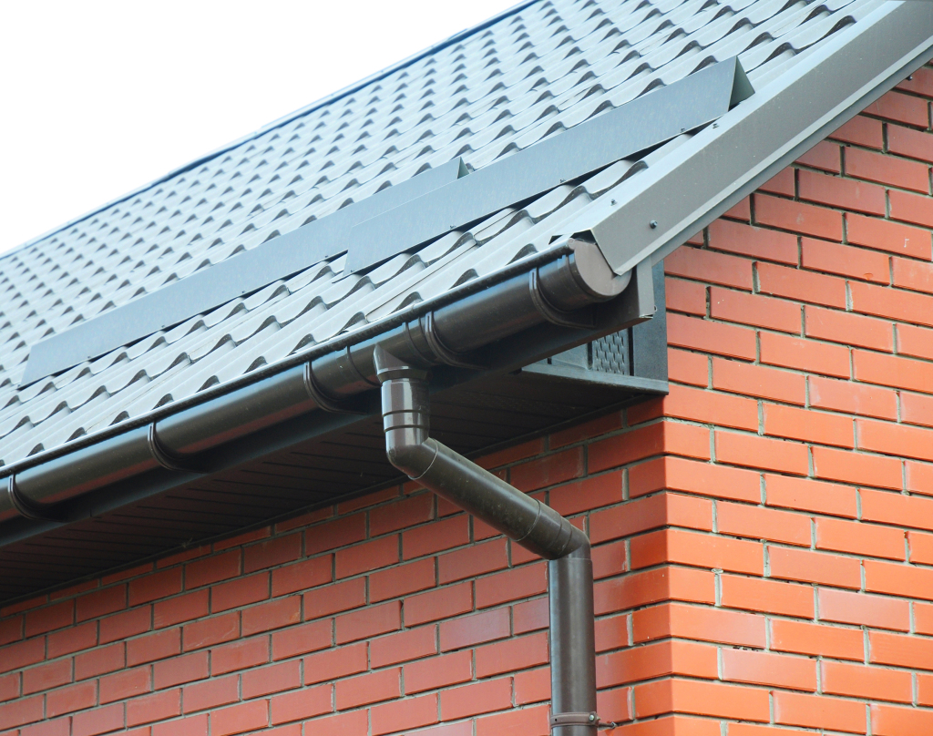 Gray metal rain gutter system with downspout on brick house with tiled roof