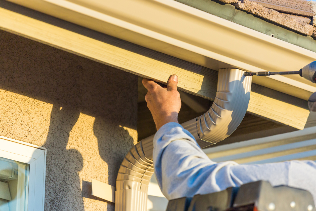 Worker installing white gutter system on residential home exterior roof edge