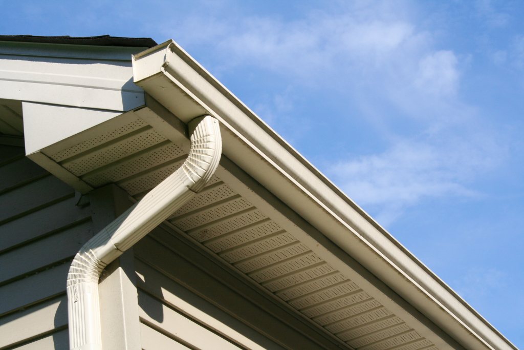 White vinyl gutters and downspout installed on house eaves against blue sky