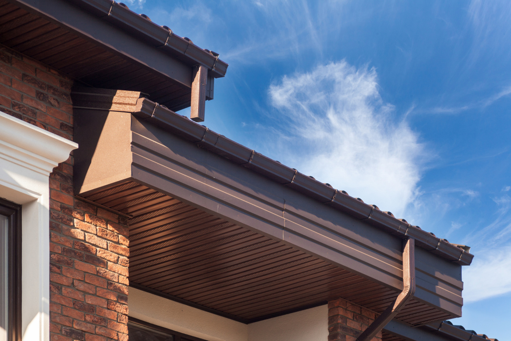 Modern house roof eaves with wooden soffits and brick walls against blue sky