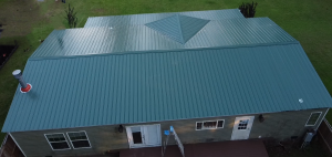 Aerial view of house with blue metal roof and gray siding surrounded by green lawn