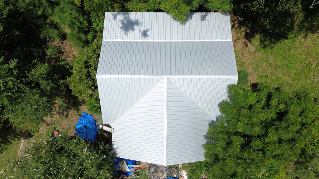 Aerial view of white metal roof building surrounded by green trees and forest
