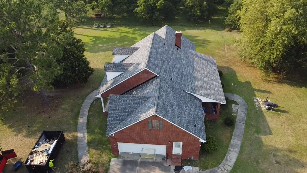 Aerial view of red brick house with gray shingle roof surrounded by green trees