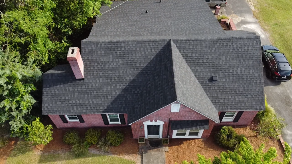 Aerial view of red brick house with gray shingle roof and brick chimneys