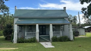 White vintage farmhouse with green metal roof and front porch in rural setting