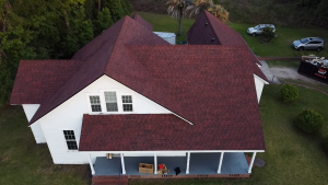 Aerial view of white house with red shingle roof and covered porch