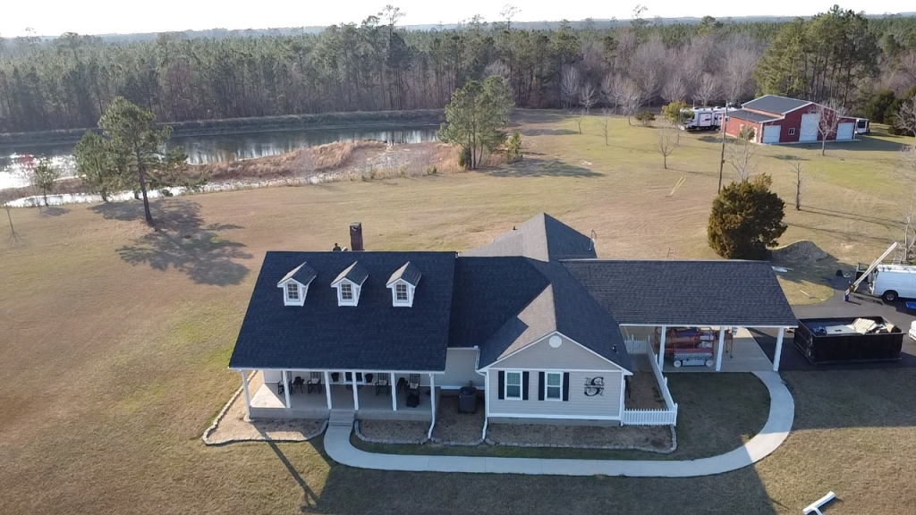Aerial view of white farmhouse with dark blue roof and dormer windows on rural property