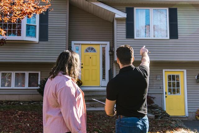 Young couple viewing gray house with yellow front door and black shutters