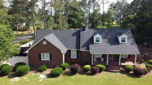 Aerial view of red brick house with gray shingle roof and landscaped yard