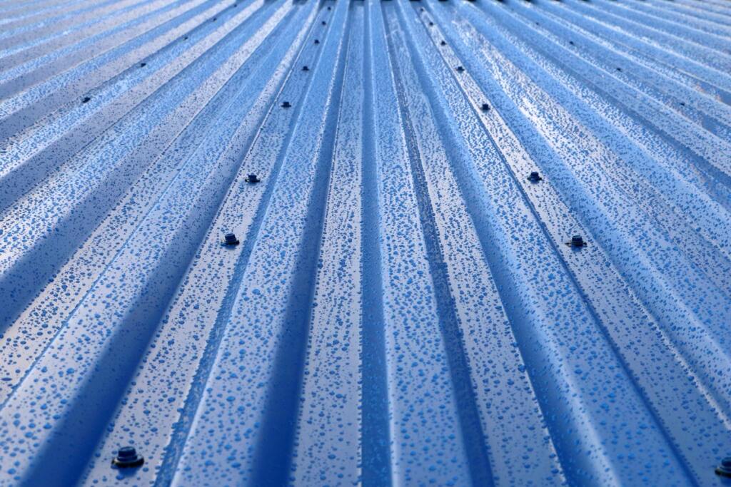 Blue metal roof with water droplets and visible screws creating parallel lines pattern