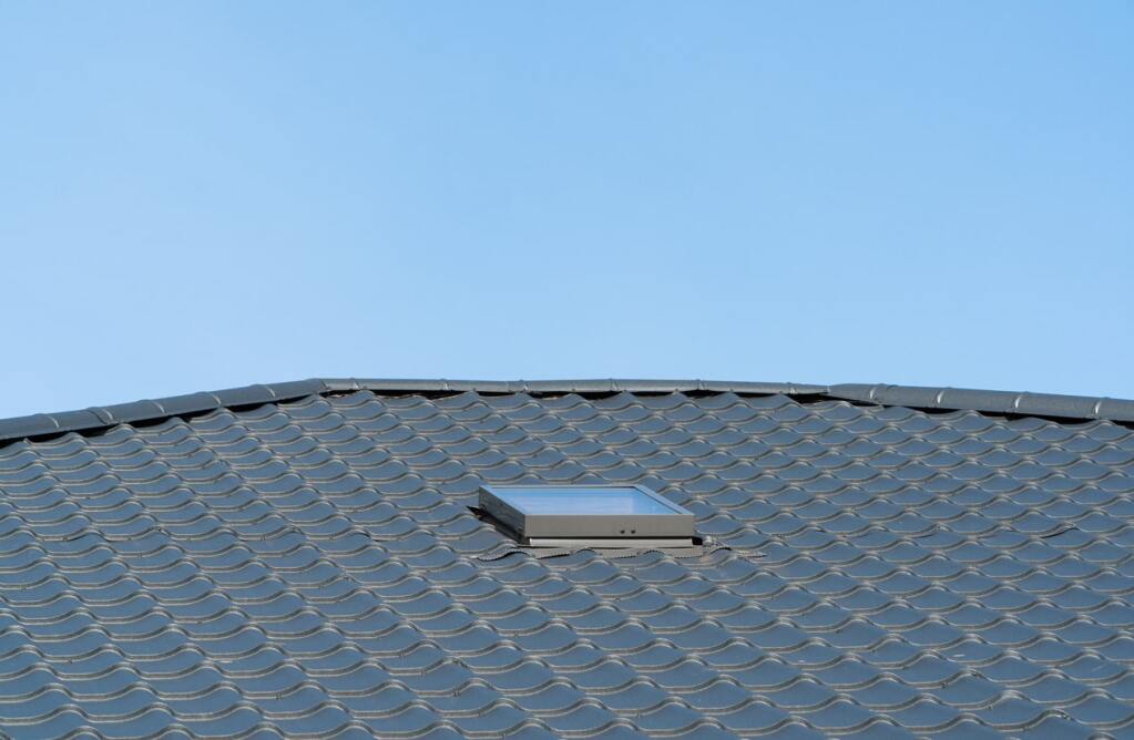 Gray clay tile roof with open skylight window against clear blue sky